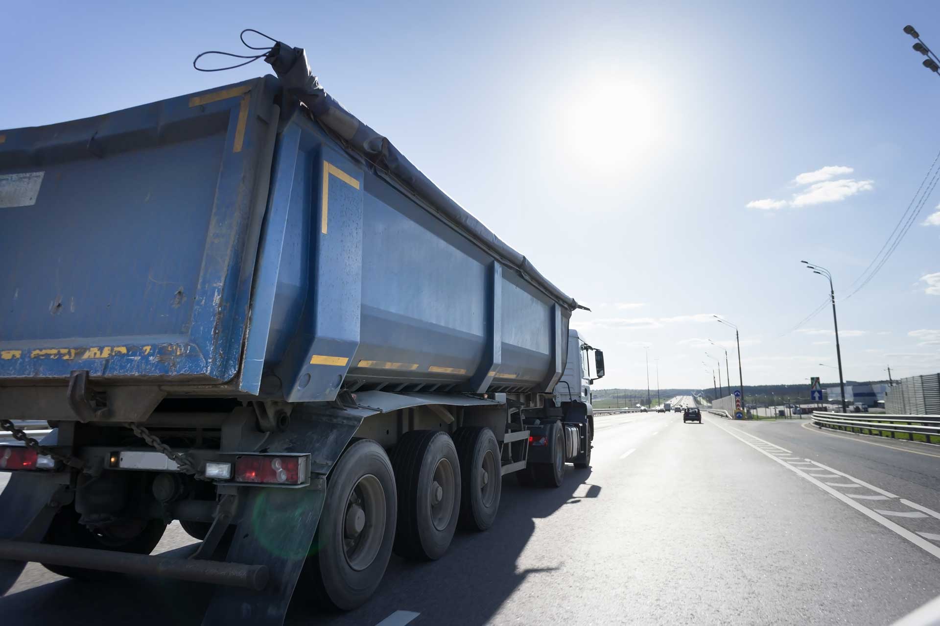 Blue dumpster truck driving down the road on a sunny day