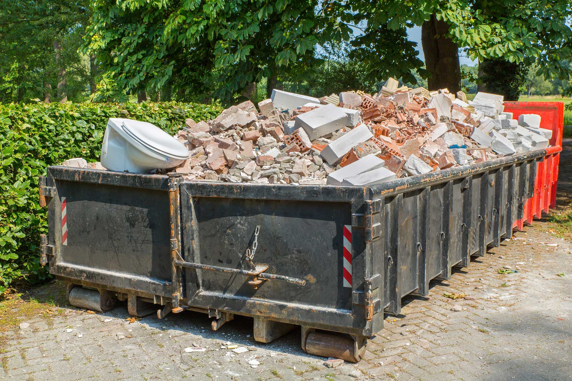 Black dumpster full of bricks, cinderblocks and other construction debris